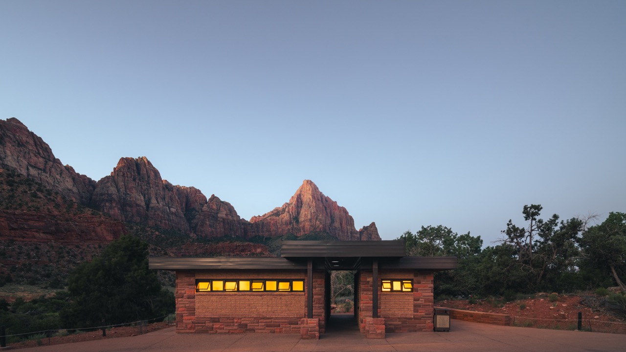 A low stone visitor building below red cliffs at dusk